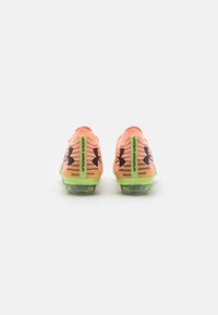 Scarpe da calcio arancioni brillanti con accenti neri, caratterizzate da una superficie testurizzata, suole verdi e un marchio sul tallone. Progettate per la trazione.