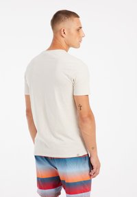 Lichtbeige t-shirt met korte mouwen en een ronde halslijn, gecombineerd met multicolor gestreepte zwembroek met blauwe, oranje en rode patronen.