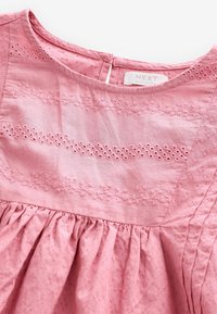 Lyserød kjole med rund halsudskæring, broderede blomsterdesigns, textureret stof og gennemsnit i bunden med knaplukning bagpå.
