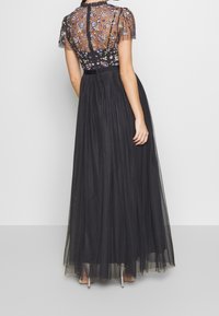 Schwarzes Maxikleid mit einem durchsichtigen, bestickten Oberteil, das farbenfrohe Blumenmuster aufweist. Fließender Tüllrock mit gepunkteter Textur. Elegantes Rückendesign.
