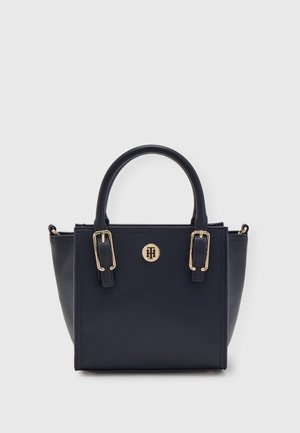 Navy blue structured handbag with two top handles, gold-tone buckles, and a round logo emblem centered on the front panel.