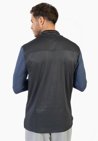 Camiseta atlética de manga larga en negro y azul, con una parte superior texturizada en negro y mangas suaves en azul. La vista trasera resalta los materiales contrastantes.