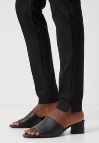 Černé sandály na podpatku s širokým otevřeným prstovým páskem, hladkou koženou texturou a blokovým podpatkem. Vytvořeno s přiléhavými černými kalhotami s bočními rozparky.