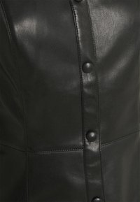 Gros plan d'un vêtement en cuir noir avec une couture verticale et des boutons ronds noirs au centre.