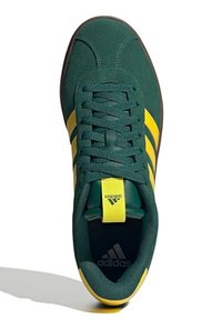 Zelené semišové tenisky s žlutým designem tří pruhů, kulatou špičkou, plochou podrážkou a polstrovaným jazykem s logem; šněrování je z texturované tkaniny.