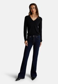 Zwarte v-halstrui met donkerblauwe flared jeans. De trui is lichtgewicht en glad; de jeans hebben contrasterende stiksels en een klassieke pasvorm.