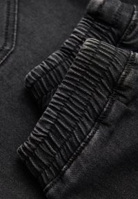 Tissu noir avec une texture côtelée aux poignets, mettant en valeur des détails de couture fins. Matériau lisse avec un design élégant et moderne.