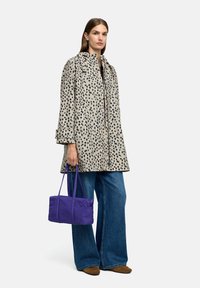 Beżowy płaszcz w czarne plamki, zapinany z przodu, dwa kieszenie na piersi, szerokie rękawy, w połączeniu z niebieskimi dżinsami w dzwony i fioletową torebką.