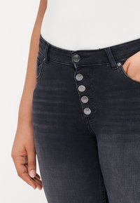 High-waisted black denim jeans with a smooth texture, featuring a five-button fly, five pockets, and subtle fading along the legs.