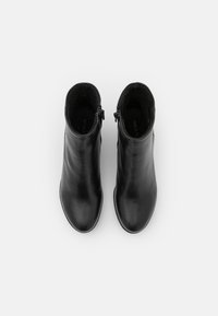Une paire de bottes noires en cuir à mi-mollet avec des zips sur les côtés, vues de dessus sur un fond blanc uni.