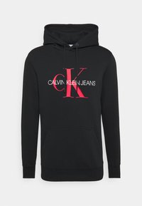 Felpa nera realizzata in tessuto morbido, con tasca frontale e cappuccio con cordino. Sul davanti è presente il logo in bold rosso e bianco "CALVIN KLEIN JEANS".