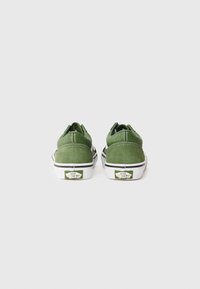 Une paire de baskets Vans vertes vues de l'arrière, montrant des semelles en caoutchouc blanches avec le logo "Vans Off The Wall" sur chaque talon.