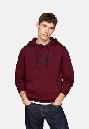 Sudadera burdeos con cordones y bolsillo frontal, que presenta un gráfico de logo en azul contrastante. Textura de punto y puños y bajo acanalados.