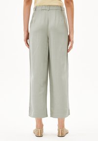 Helle grüne, fließende, weit geschnittene Hosen mit elastischem Bund. Sanfte Textur und cropped Design, kombiniert mit hellbeigen Schuhen.