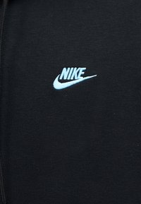 Μαύρο ύφασμα με ανοιχτό μπλε λογότυπο Nike και σύμβολο επάνω, κεντημένα στο κέντρο μπροστά.