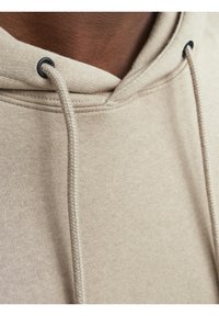 Tanskleurige hoodie met een zachte textuur, voorzien van een voorste kangoeroezak, verstelbare trekkoorden en zwarte kunststof oogjes voor de hoodietrekken.