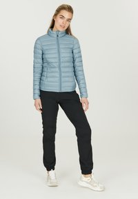 Lyseblå, quiltet jakke med standkrave og fuld lynlås, parret med sorte tapered bukser og lyse sneakers. Glat tekstur overalt.