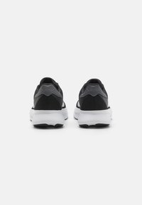 Une paire de baskets noires et grises avec des semelles blanches, vues de l'arrière sur un fond blanc uni.
