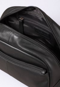Black leather backpack interior with a zippered pocket and a smooth, textured wall. Features a label with embossed text.