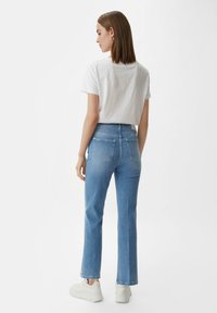 Niebieskie dżinsy o wysokim stanie, proste nogawki i dwie tylne kieszenie, w połączeniu z białą koszulą z krótkim rękawem i białymi sneakersami.