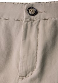 Beige bomullstygbyxor med framficka, en svart knapp och synliga sömnadsdetaljer. Slät textur med en avslappnad design.