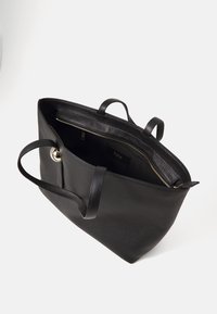 Sac fourre-tout en cuir noir avec deux poignées. Surface texturée, ouverture sur le dessus et poche zippée à l'intérieur. Doté d'une fermeture à bouton poussoir doré.