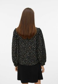 Blusa nera a fiori con maniche a sbuffo; presenta piccoli motivi floreali multicolori, tessuto morbido e una vestibilità rilassata. Abbinata a una gonna nera.