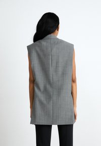 Harmaa liivi ilman hihoja, jossa on pystysuorat raidat, mukautettu istuvuus, rakenteelliset olkapäät ja siisti takasauma. Sujuva kankaan tekstuuri.