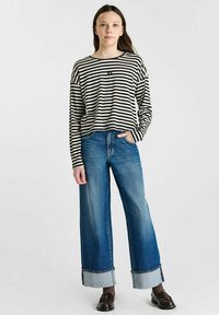 Zwart-witte gestreepte lange mouwen shirt gecombineerd met high-waisted wijde lichtblauwe jeans, met omgeslagen mouwen en donkere schoenen.