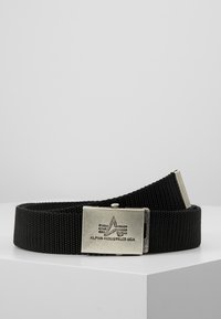 Svart vävd tygbälte med en silvrig metallspänne som har en logotyp och graverad text "ALPHA INDUSTRIES USA." Justerbar längd.