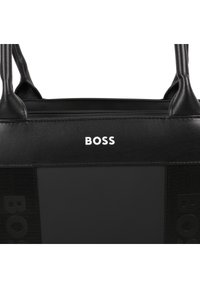 Saco tote preto feito de couro e tecido, apresentando o nome da marca "BOSS" em branco na parte da frente e acabamentos texturizados nas laterais.