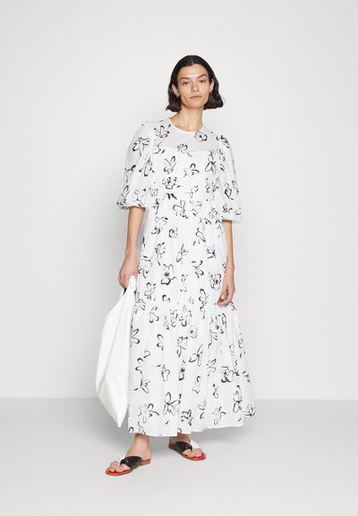 Λευκό μακρύ φόρεμα με λουλούδια, φουσκωτά μανίκια, μαζεμένη μέση και φούστα με στρώσεις. Συνδυάζεται με μαύρες και κόκκινες σαγιονάρες και λευκή τσάντα.