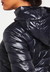 Mørk navy dunjakke med en blank finish, der har en høj krave og quiltede syninger for isolering og tekstur. Slidstærkt stofdesign.