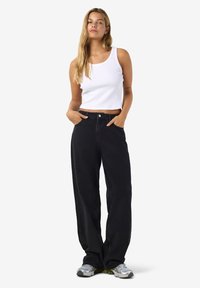 Crne široke traperice visokog struka, uparene s bijelom rebrastom uskom majicom bez rukava. Nošene s sivim sportskim tenisicama, ruke u džepovima.