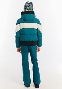 Tyrkysová pufrová bunda s bielymi a čiernymi pruhmi, pridruženou kapucňou a elastickými manžetami. Úplne doladená s nohavicami s rozšíreným strihom a čižmami.