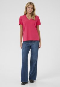 T-shirt rose à col en V avec des manches courtes, associé à un jean en denim bleu à jambes larges. Le tissu semble lisse et léger.