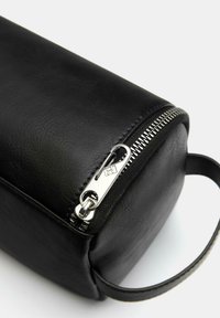 Borsa nera in ecopelle con forma cilindrica. Presenta una zip argentata e una maniglia laterale. Texture liscia senza pattern visibili.