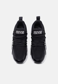 Μαύρα αθλητικά παπούτσια με άνω μέρος από δίχτυ με γυαλιστερές λεπτομέρειες, στρογγυλά κορδόνια και τη φράση "VERSACE JEANS COUTURE" στη γλώσσα.