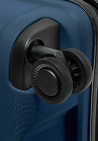Nahaufnahme von zwei schwarzen Spinner-Rädern, die an der strukturierten Ecke eines blauen Hartschalenkoffers befestigt sind.