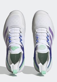Białe buty sportowe z siateczkową cholewką, fioletowymi i niebieskimi akcentami, zielonymi detalami oraz teksturowaną podeszwą. Posiadają wyściółkę przy kołnierzu i sznurówki.