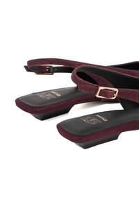 Dark burgundy suede slingback shoes with a small solid black heel, featuring a buckle strap and a black insole with gold branding.