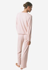 Lichtroze loungewear set met een textuur van ribbelbreiwerk. De top heeft een ontspannen pasvorm met lange mouwen, en de broek heeft een rechte pijp.