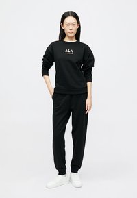 Zwarte sweatshirt met wit logo, gecombineerd met zwarte joggingbroek en witte sneakers. Glad materiaal, relaxed fit. Eenvoudig ontwerp.