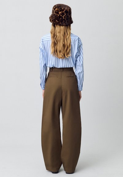 Camisa de rayas azul y blanca combinada con pantalones marrones sueltos de tiro alto. Un sombrero tipo bucket con estampado de leopardo complementa el peinado.