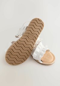 Witte platte sandalen met een getextureerde tan zool, voorzien van gerimpelde bandjes en een zachte voetbed. Eenvoudig ontwerp zonder zichtbare hardware.