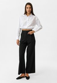 Witte, cropped, knoop-overhemd met lange mouwen en een relaxte pasvorm, gecombineerd met hoge taille, zwarte wijde broek met een knoop aan de voorkant.