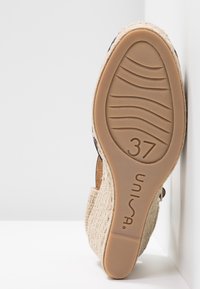 Sandale compensée avec une tige en fibre naturelle tissée et une semelle en caoutchouc beige. Taille 37 marquée sur la semelle. Fini lisse, design ouvert au talon.