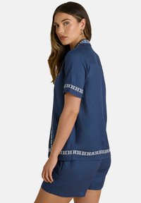 Marineblauw tweedelig set bestaande uit een geknoopte top met korte mouwen en een witte patroonrand, en bijpassende shorts met omslagen. Gladde textuur.