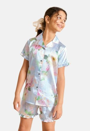 Lány világoskék virágos rövid ujjú szatén pizsamában, fodros szegéllyel, oldalra néz, bézs hajgumival a lófarokban.