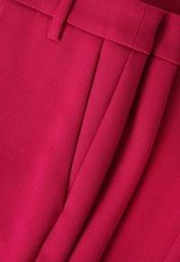 Fuchsiová tkanina s hladkým povrchem, s ostrými sklady a širokým páskem. Design zdůrazňuje upravenou siluetu.